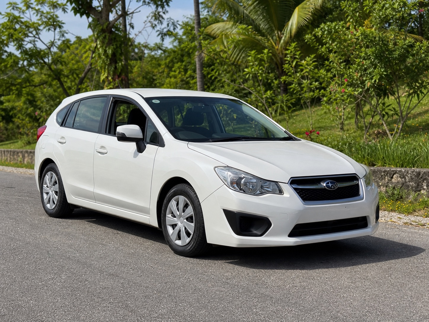 White 2016 Subaru Impreza hatchback parked on a Jamaica road with tropical greenery